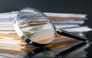 Private investigator examining estate and probate documents with a magnifying glass during a fraud investigation